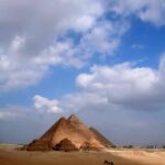 The iconic Pyramids of Giza stand majestically under a bright blue sky with scattered clouds.